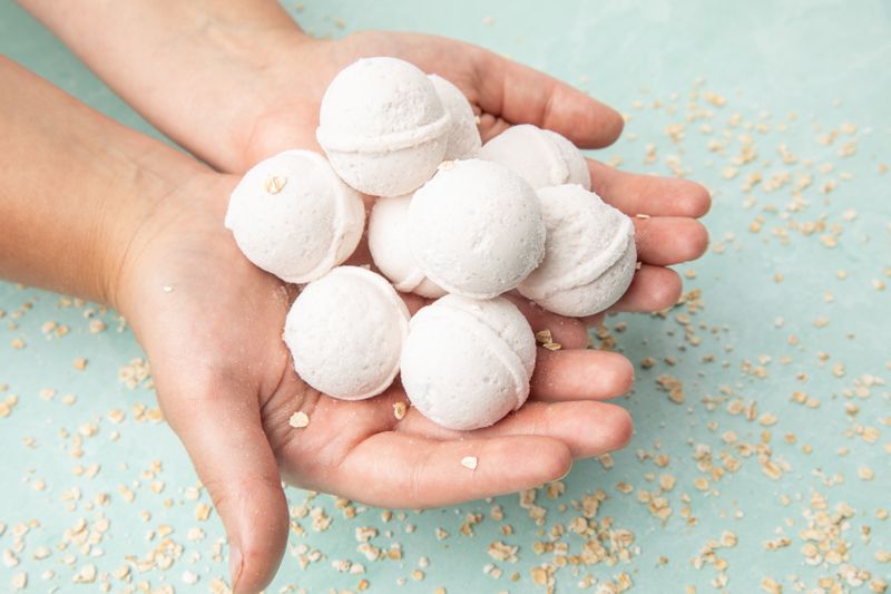 Woman holding nine My Mommy Wisdom Oatmeal Milk & Honey Bath Bombs with scattered dry oats under her hands