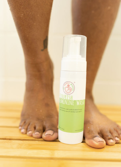 Black woman standing next to a bottle of My Mommy Wisdom Flourish: Feminine Wash